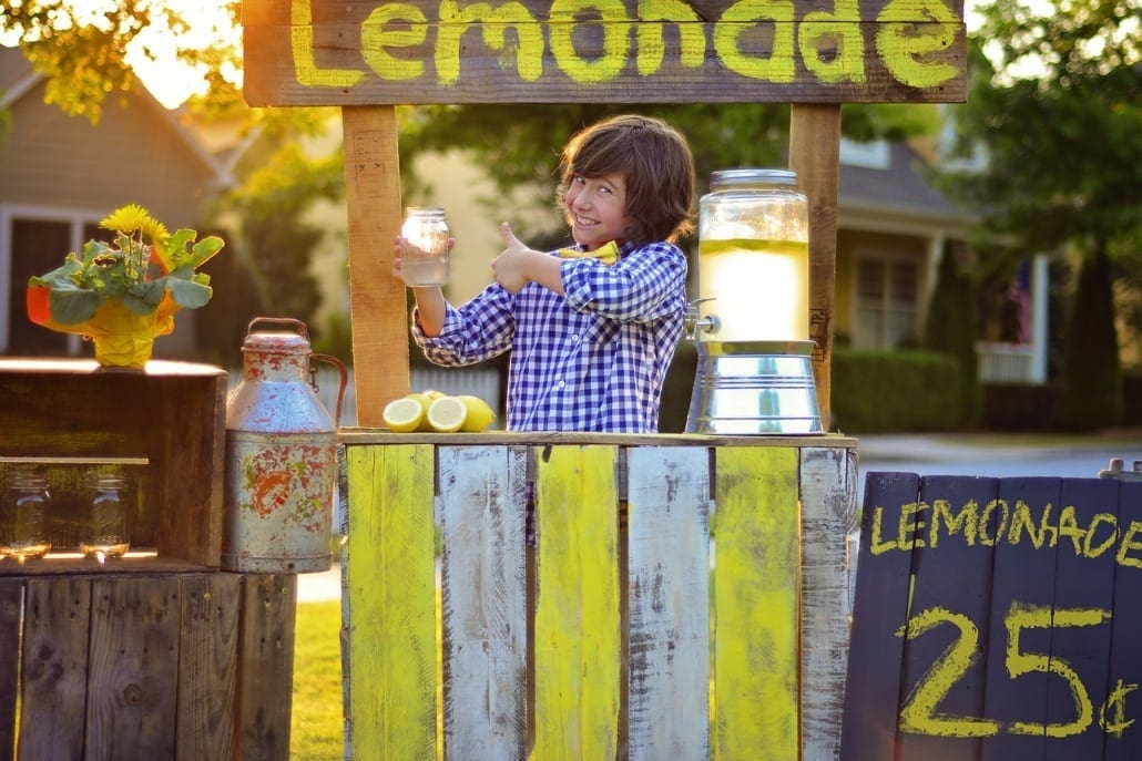 Young boy smiling holding up a glass of lemonade at his lemonade stand